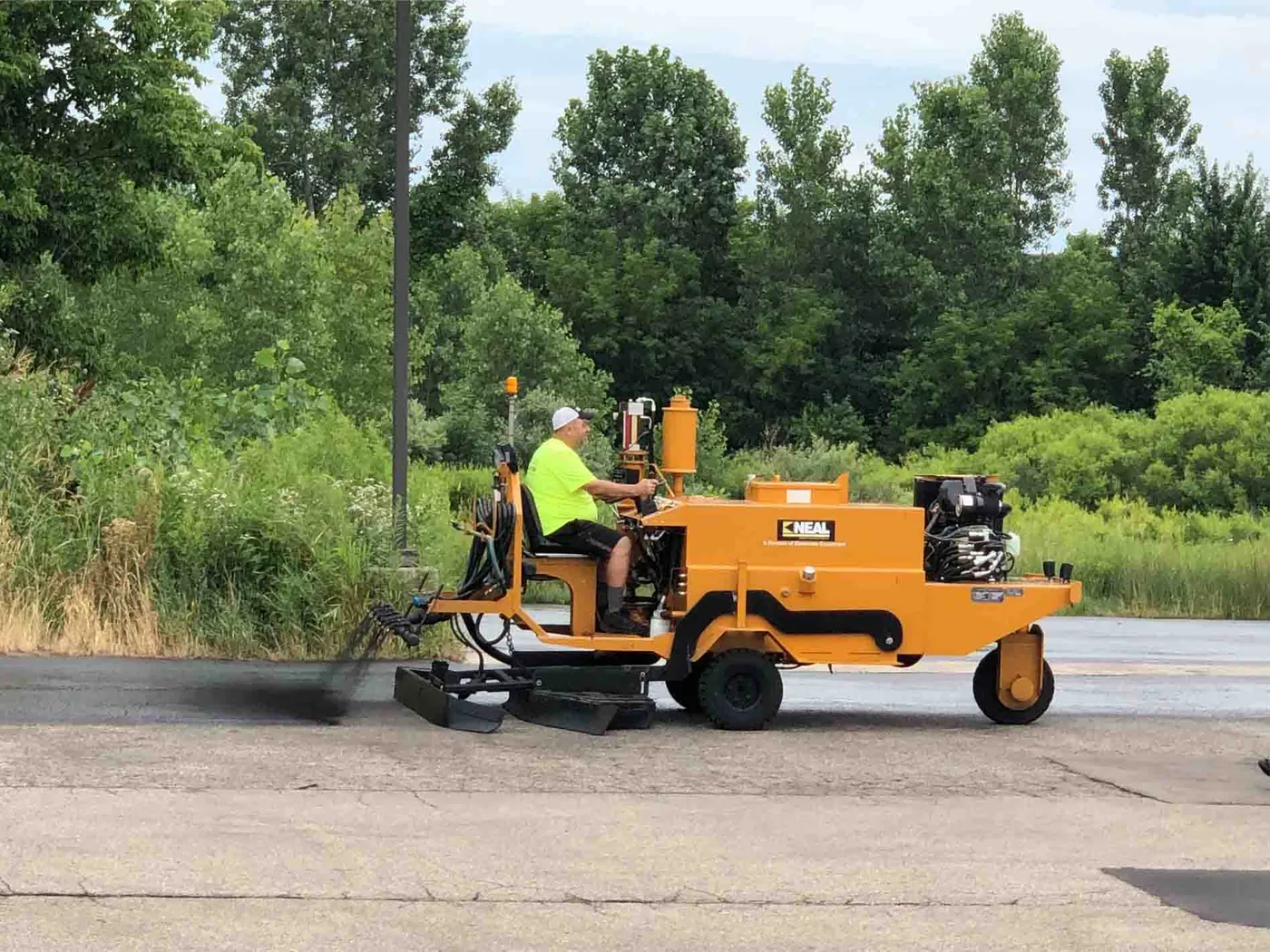 Ride-on squeegee machine spreading fresh black seal coat across an asphalt parking lot